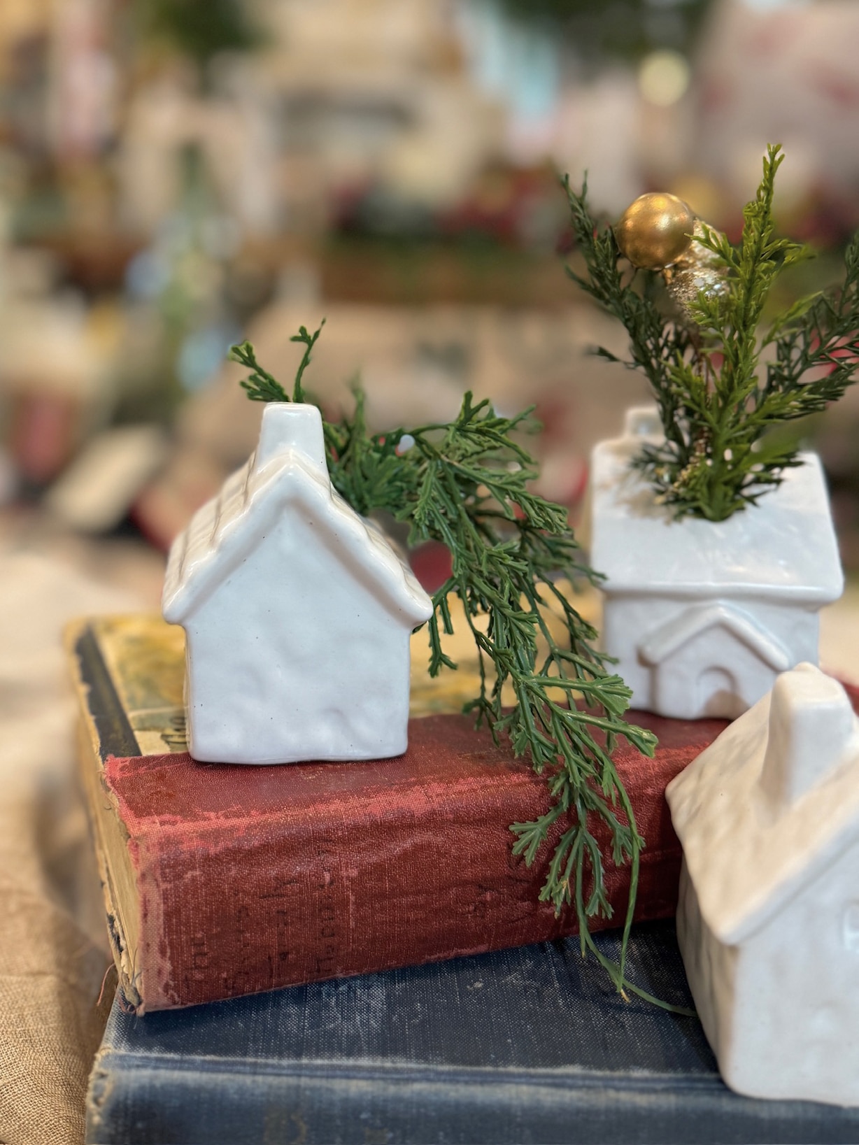 Close-up of small cream stoneware house candle holder decorated with greenery and gold berries.