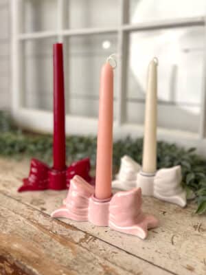 Pink, red, and white bow taper candle holders styled together with Evoke taper candles on a rustic wood surface.