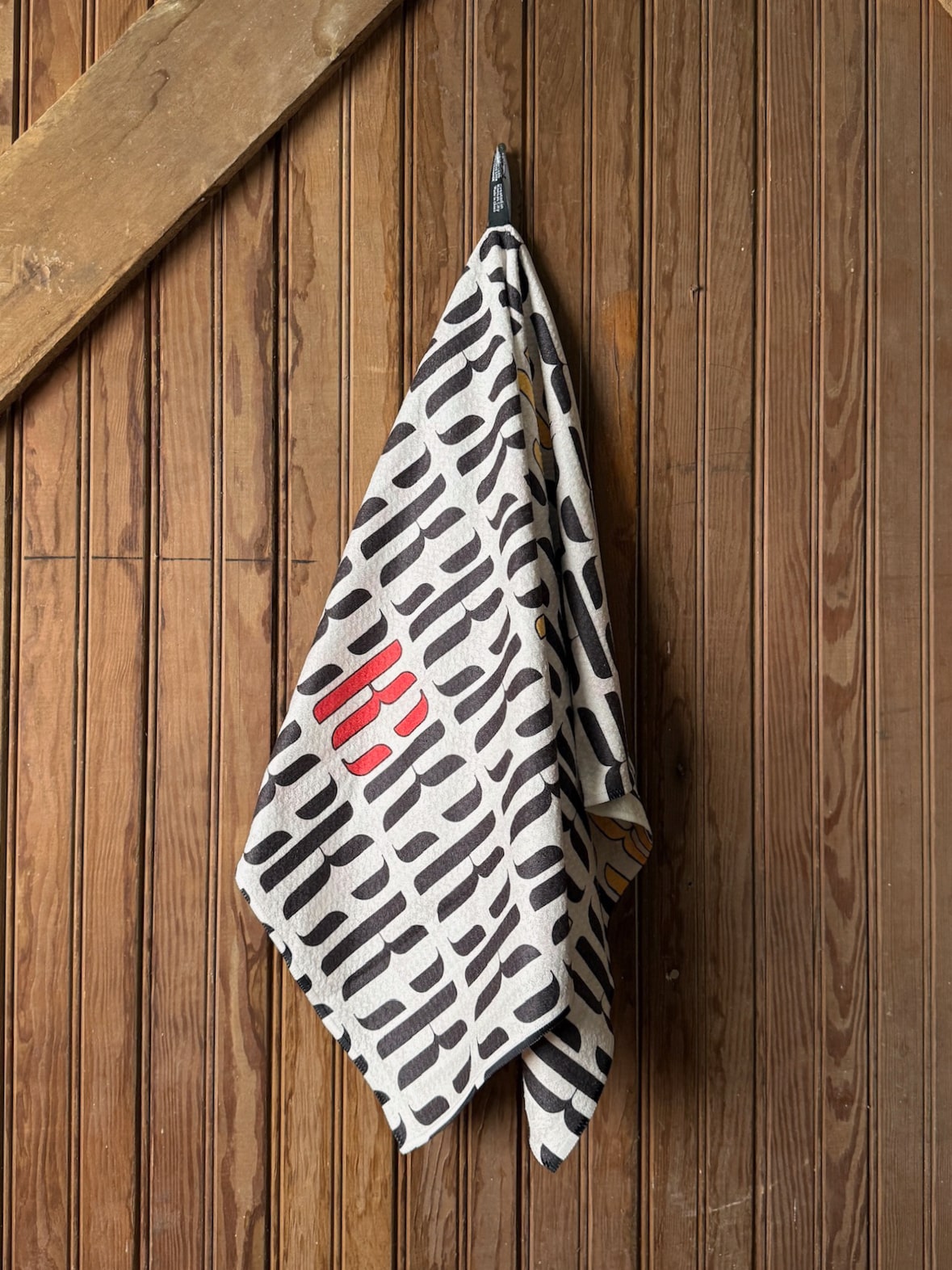 Black and white patterned microfiber tea towel with red Chiefs player illustrations, hanging from a hook on a wooden wall.