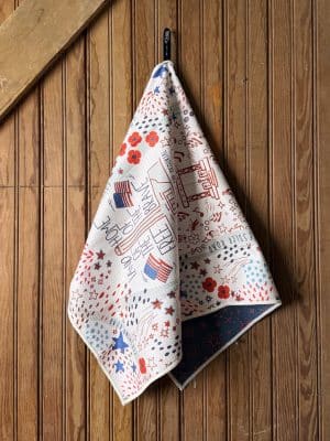 Patriotic microfiber tea towel featuring Kansas City WWI Museum design with red poppies and American flags, hanging neatly on a wooden wall.