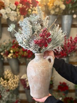 A front view of the tuscan terracotta vase styled with frosted winter greenery and red berries.