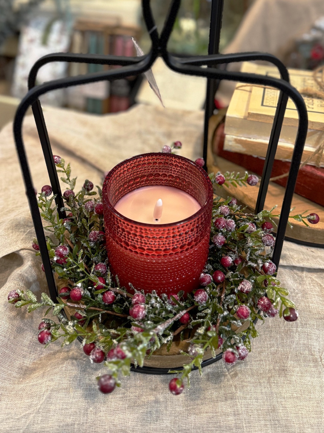 Black metal open frame lantern with wood base styled with a red dotted glass flameless candle and frosted berry candle ring.