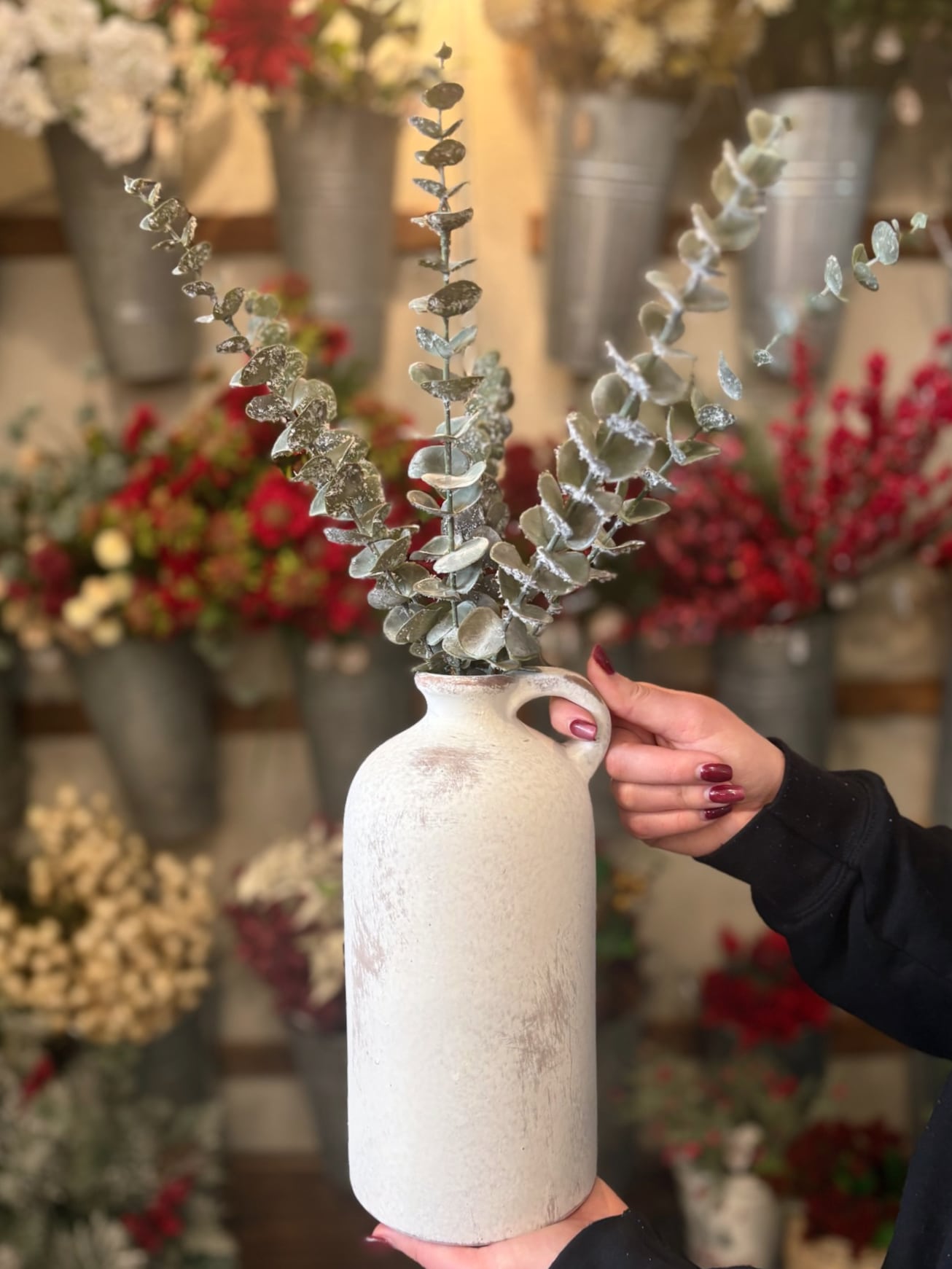 be-made-hays-ks-large-single-handle-rustic-white-vase-with-greenery Large Single Handle Rustic White Vase with frosted eucalyptus stems displayed in hand.