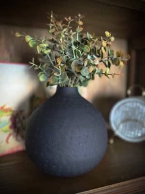 Small matte black round vase with hand-punched texture and sculptural shape, styled as a decorative accent on a tabletop.
