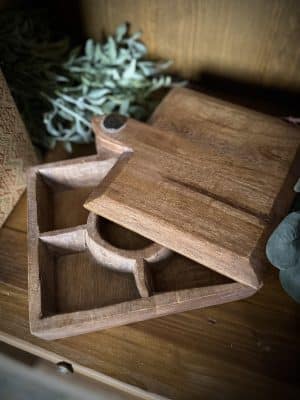 Close-up of a square wood storage box with sliding lid partially open, revealing four divided compartments.