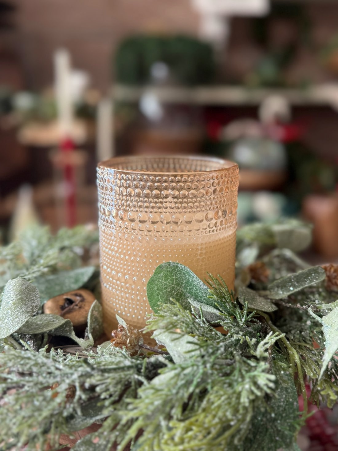 Champagne dotted flameless candle displayed inside a frosted cedar and eucalyptus wreath with jingle bells.