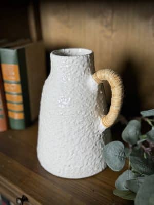 Close-up of the small ceramic vase with a speckled glaze and a rattan-wrapped handle, highlighting its texture and artisan detail.