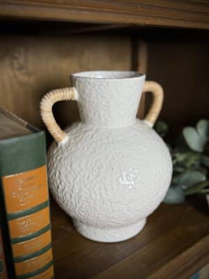 Close-up of a medium off-white ceramic vase with textured finish and two hand-wrapped rattan handles.