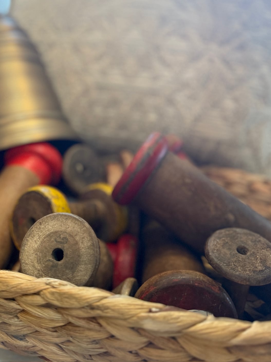 Vintage wooden spools in a woven basket, showing distressed wood, worn ends, and aged patina for rustic home styling.