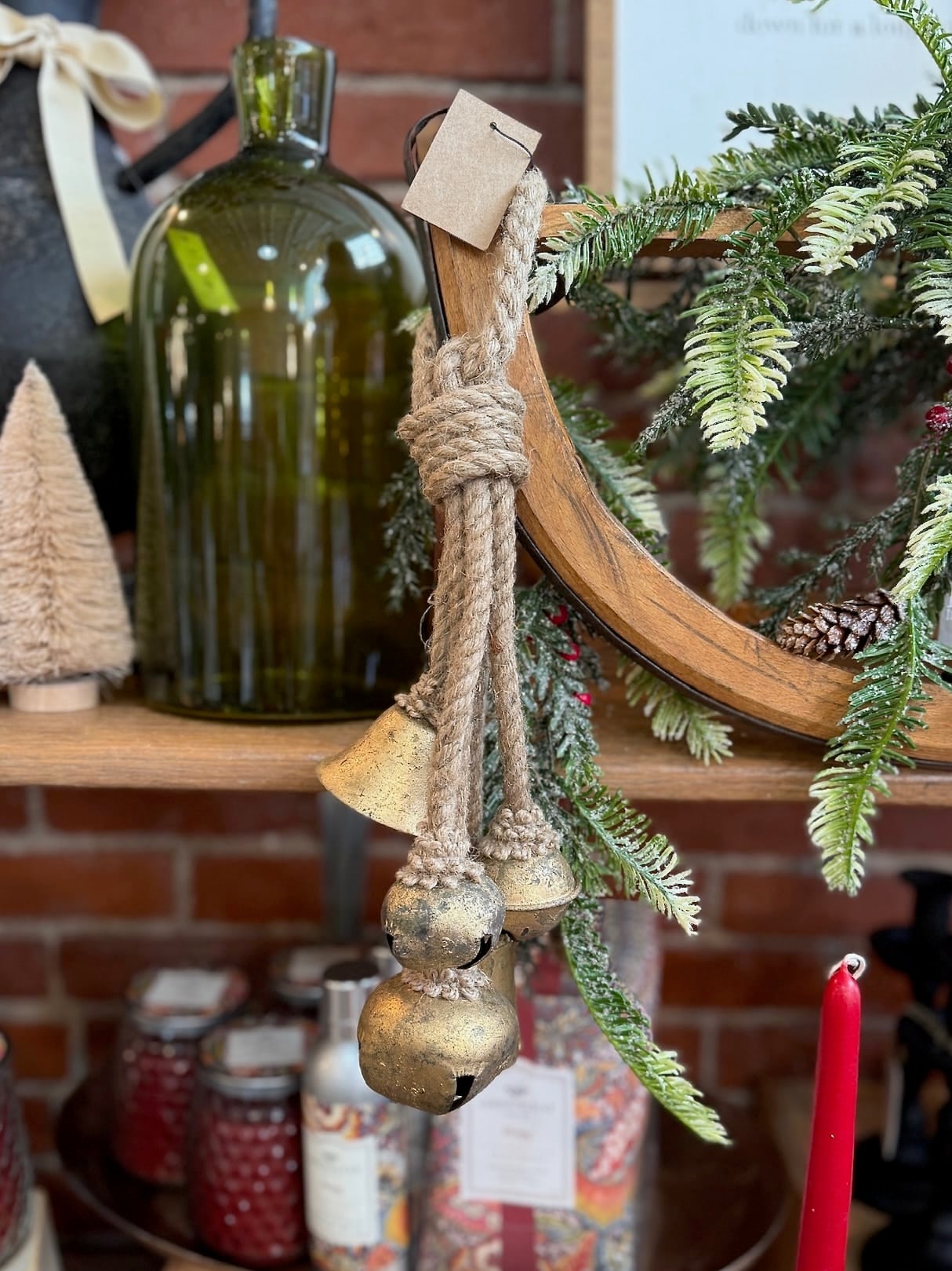 Hanging Gold Bells with rustic jute rope draped over a wooden mirror, surrounded by pine greenery and festive accents.