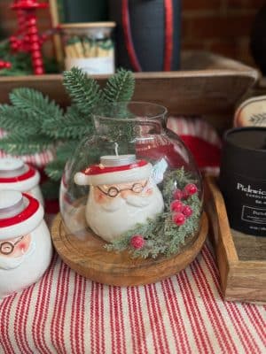 Ceramic Santa Tealight Candle Holder with glasses and red hat displayed beneath a rounded glass cloche with greenery and berries.