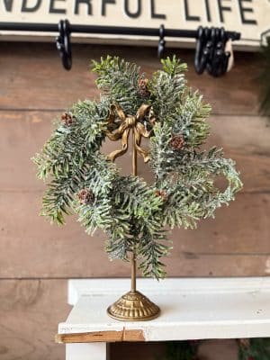 Gold Wreath Stand with Bow displaying a frosted evergreen candle ring with pinecones.