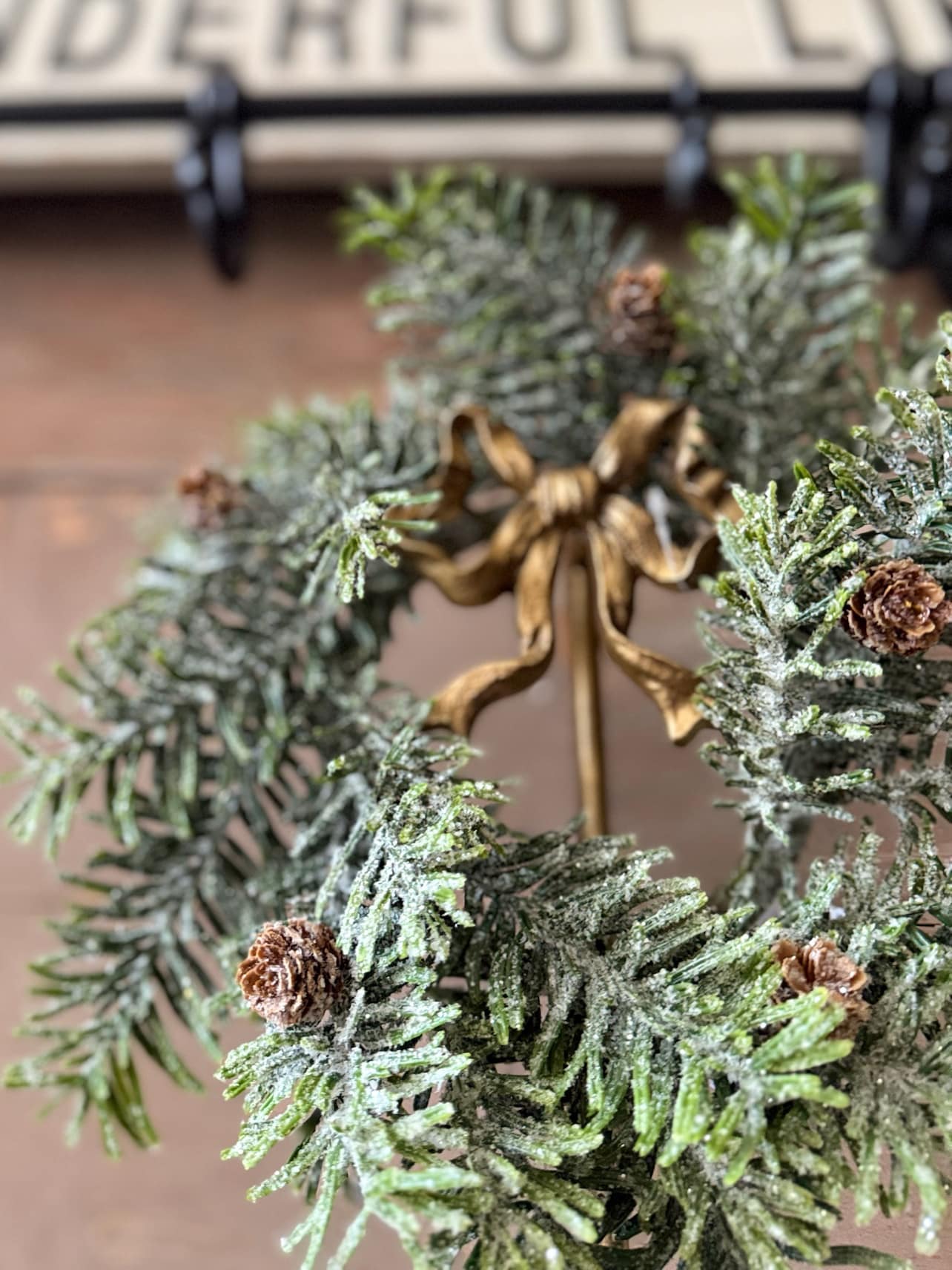 Frosted Hemlock with Pinecones Candle Ring styled on a gold wreath stand with bow.