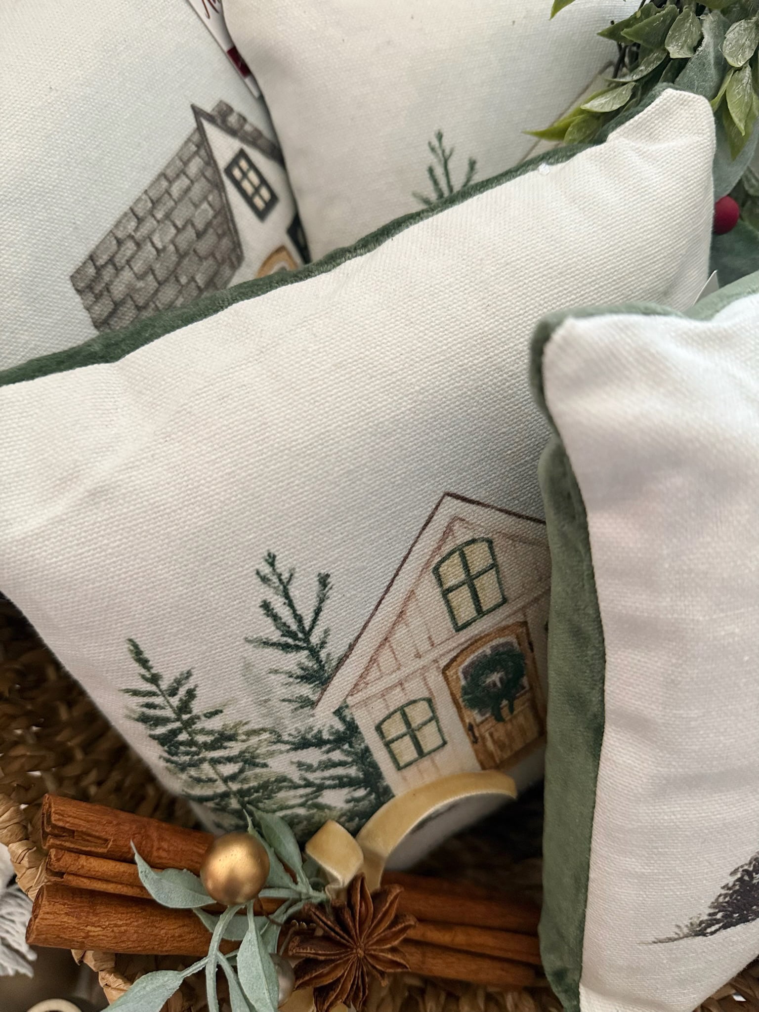 Close-up of Cozy Winter Cottage Mini Pillows with snowy cottage illustrations and pine tree designs, featuring soft cotton fronts and green velvet backs.