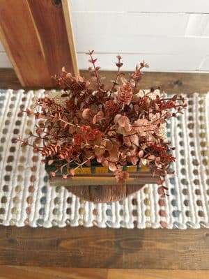 Top view of orange eucalyptus and hops orb arranged on stacked vintage books atop a wood pedestal.