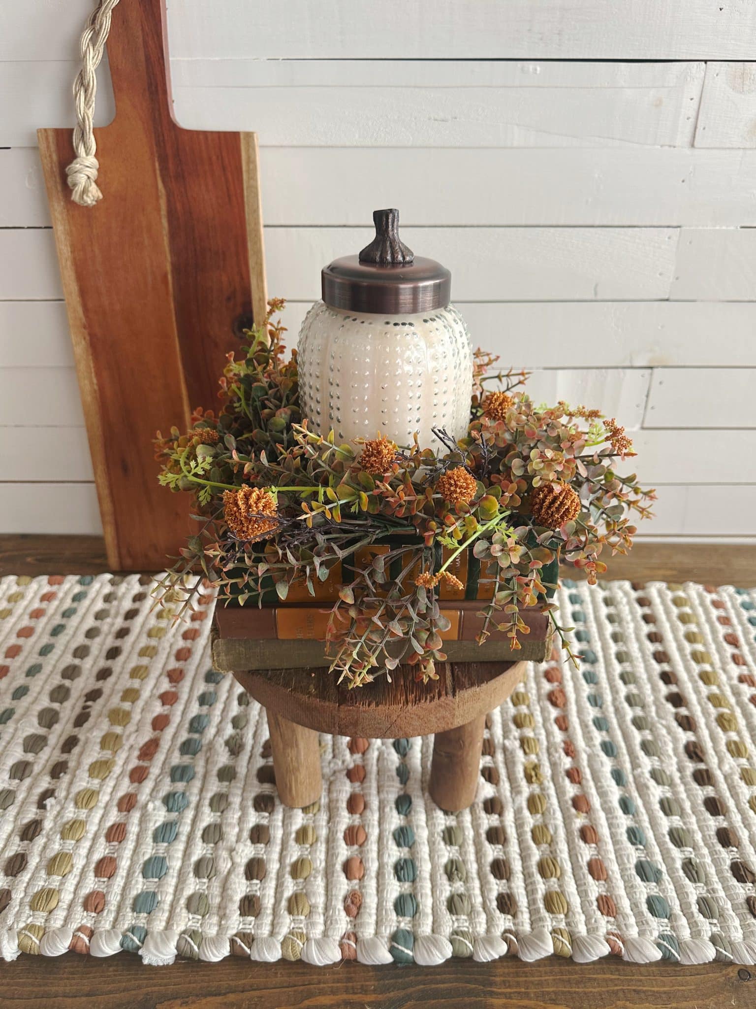 White pumpkin candle centerpiece with orange floral ring and vintage book stack on a cozy table runner.