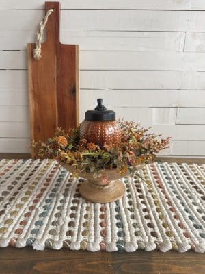 Cozy fall candle display featuring floral ring, wood bowl, and warm-toned woven table runner