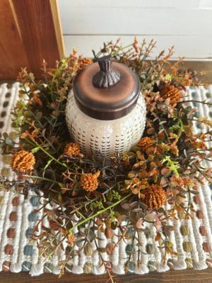 Overhead view of the Pumpkin Chata candle styled inside an orange floral ring on a wood pedestal bowl