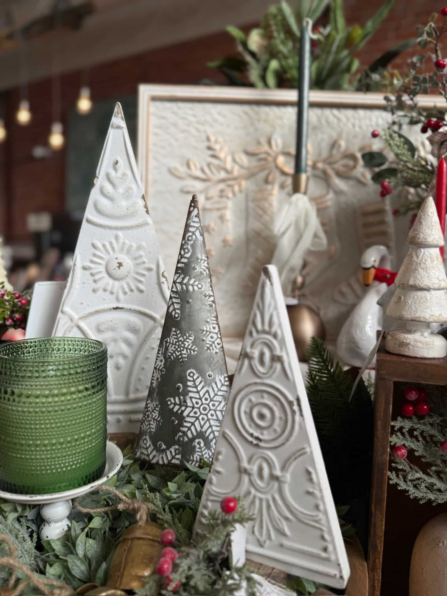 Close-up of Antique White Pressed Metal Trees with distressed detailing, displayed with a green dotted candle and winter greenery.