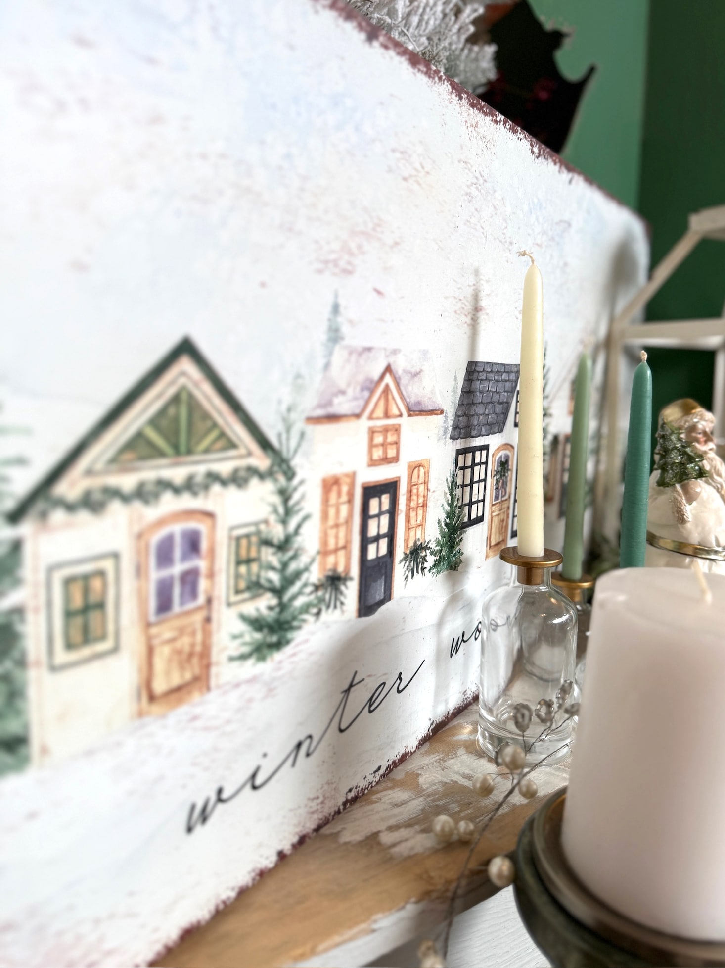 Winter Wonderland metal sign with illustrated snowy cottages and evergreen trees styled on a holiday mantel.