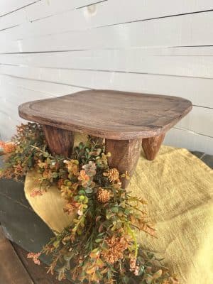 Side view of wooden stool styled with fall garland and stonewashed mustard table runner