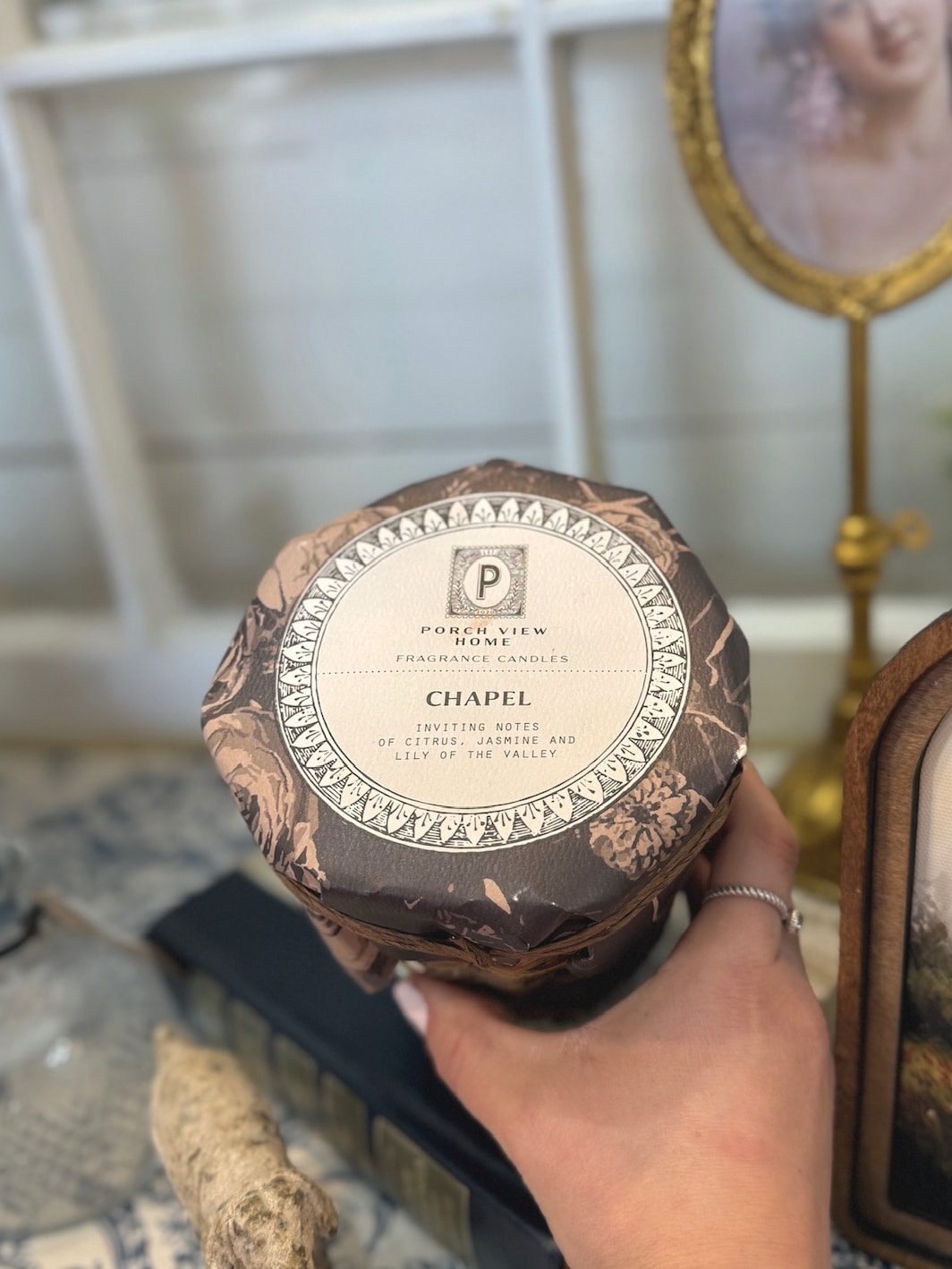 Top view of Wicker Chapel Candle with decorative label resting on vintage book stack in cozy cottage setting