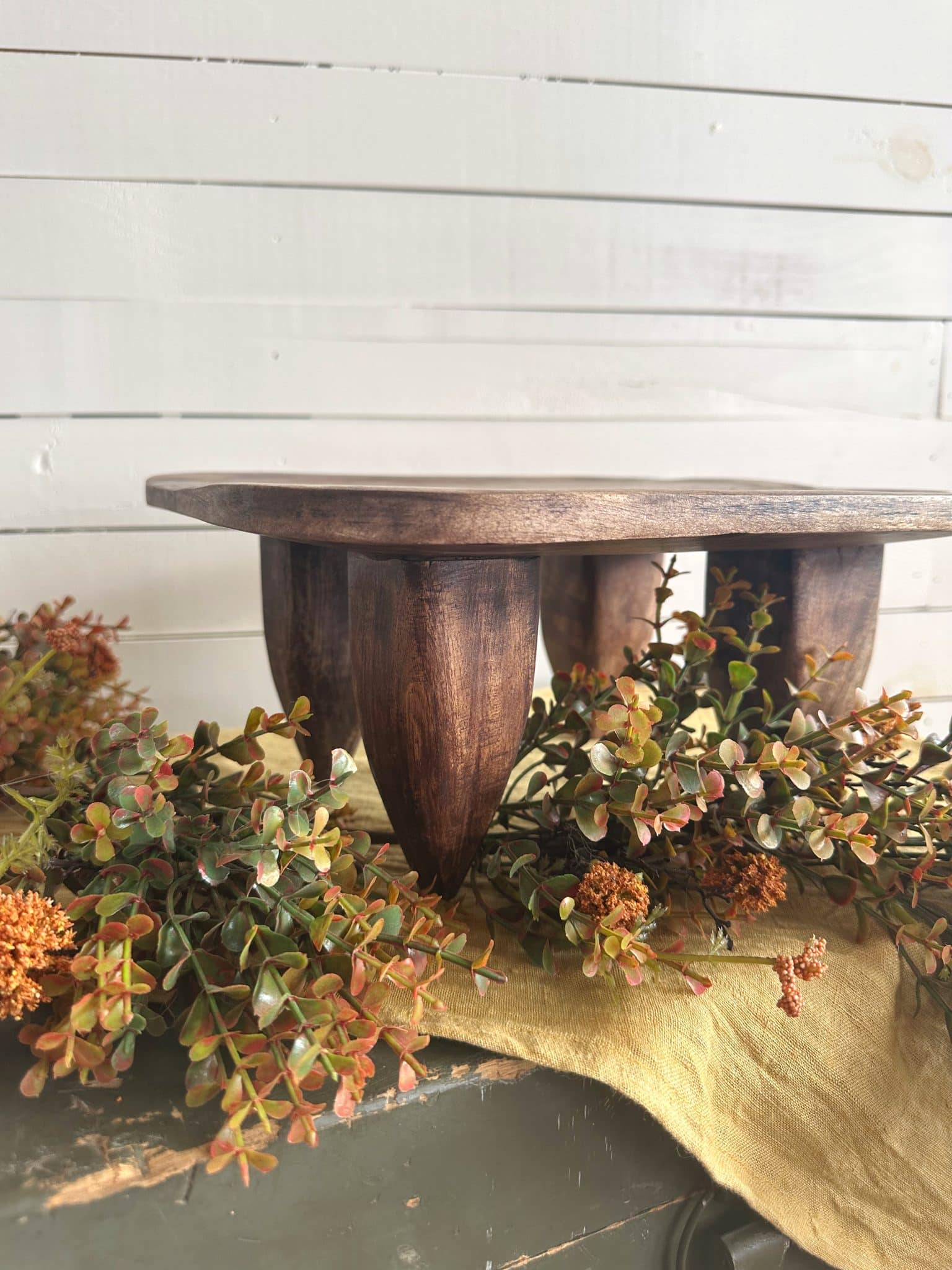 Primitive square wood stool on mustard linen runner with fall garland draped around base