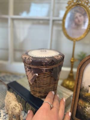 Wicker Chapel Candle in natural woven holder styled on stacked vintage books with gold mirror and cottage decor background
