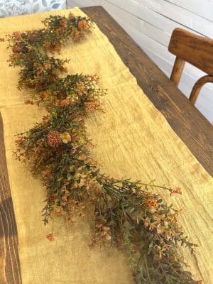 Fall garland with rust and green hues styled down a mustard linen table runner on a dark wood table