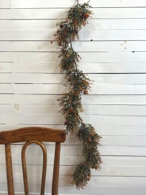 Orange pincushion faux floral garland draped beside a wooden chair on white shiplap wall