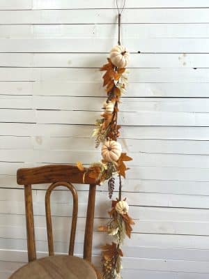 Faux fall garland with pumpkins and foliage draped beside a wooden chair