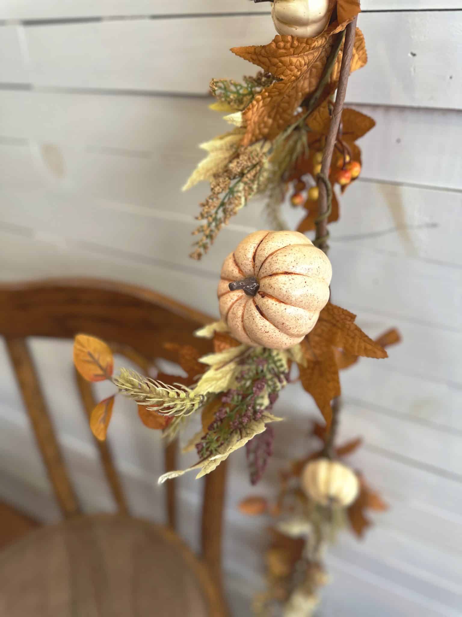 Close-up of faux autumn garland with soft orange pumpkins, leaves, and twigs