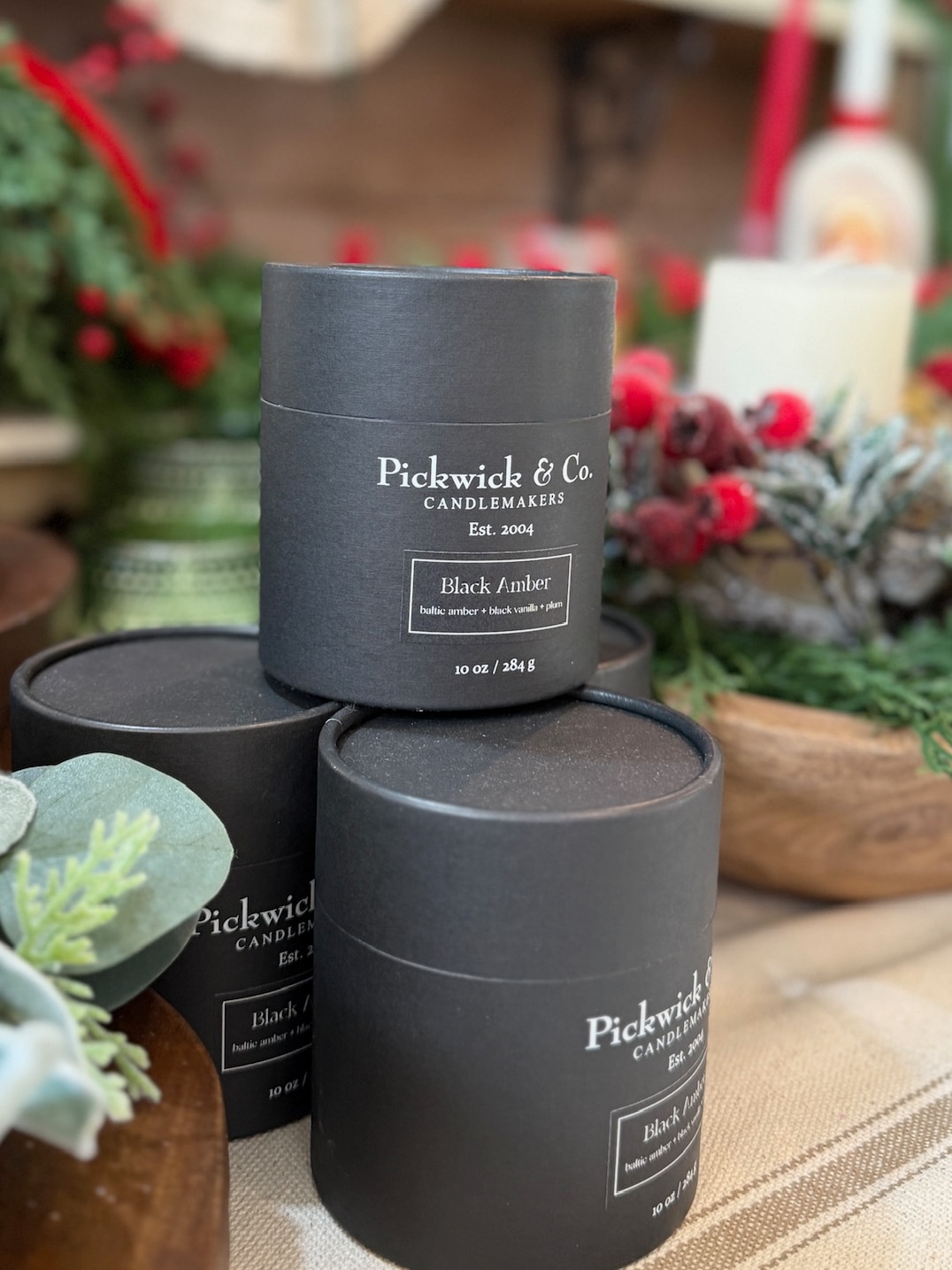 Black Amber Pickwick Candle in signature black packaging, stacked in a cozy holiday display.