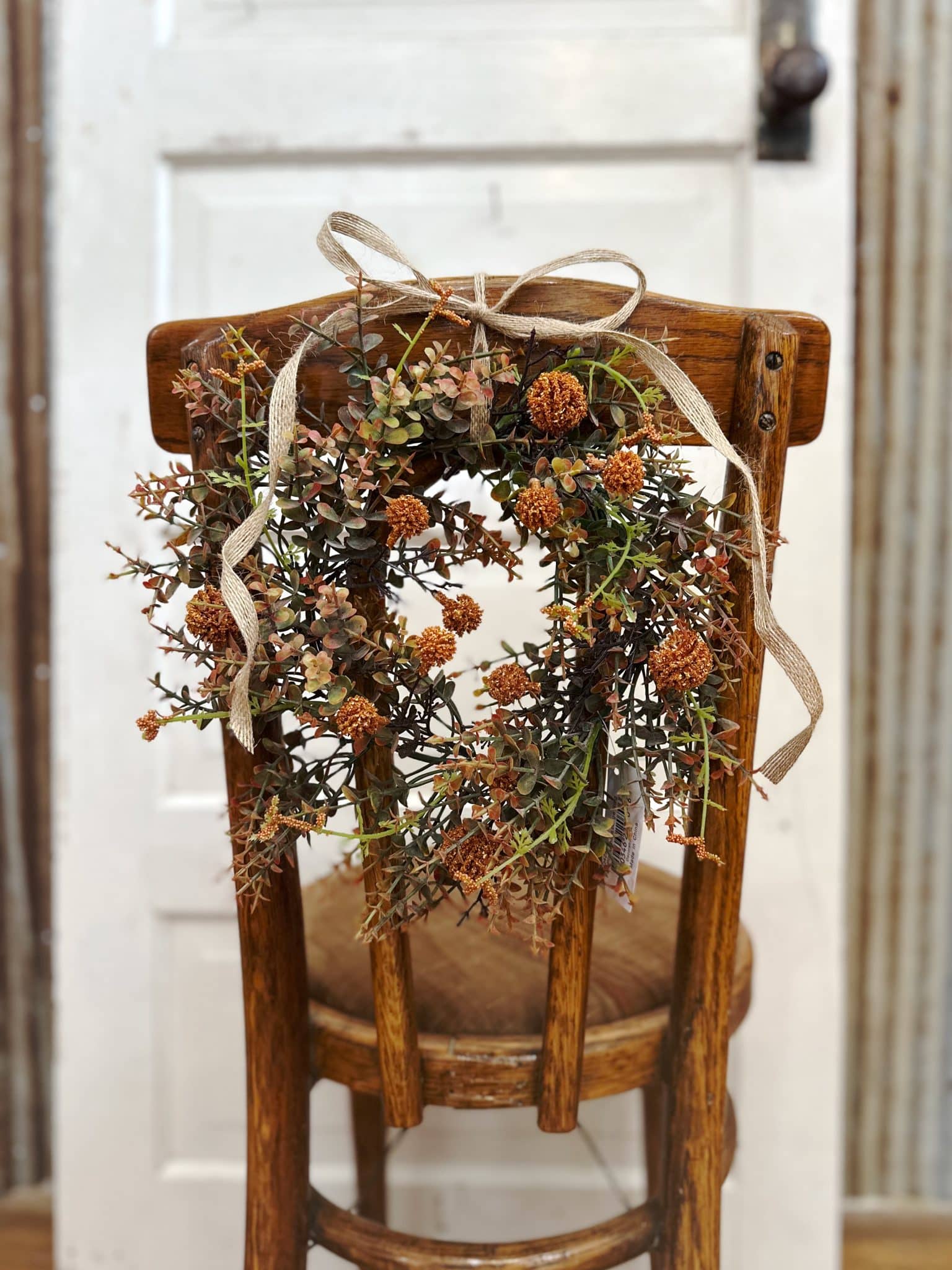 Faux fall floral candle ring with orange blooms tied with ribbon to a wooden chair
