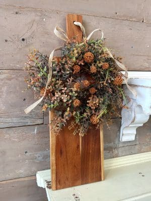 Faux fall floral ring with orange pincushion blooms tied to a wood board with rope handle