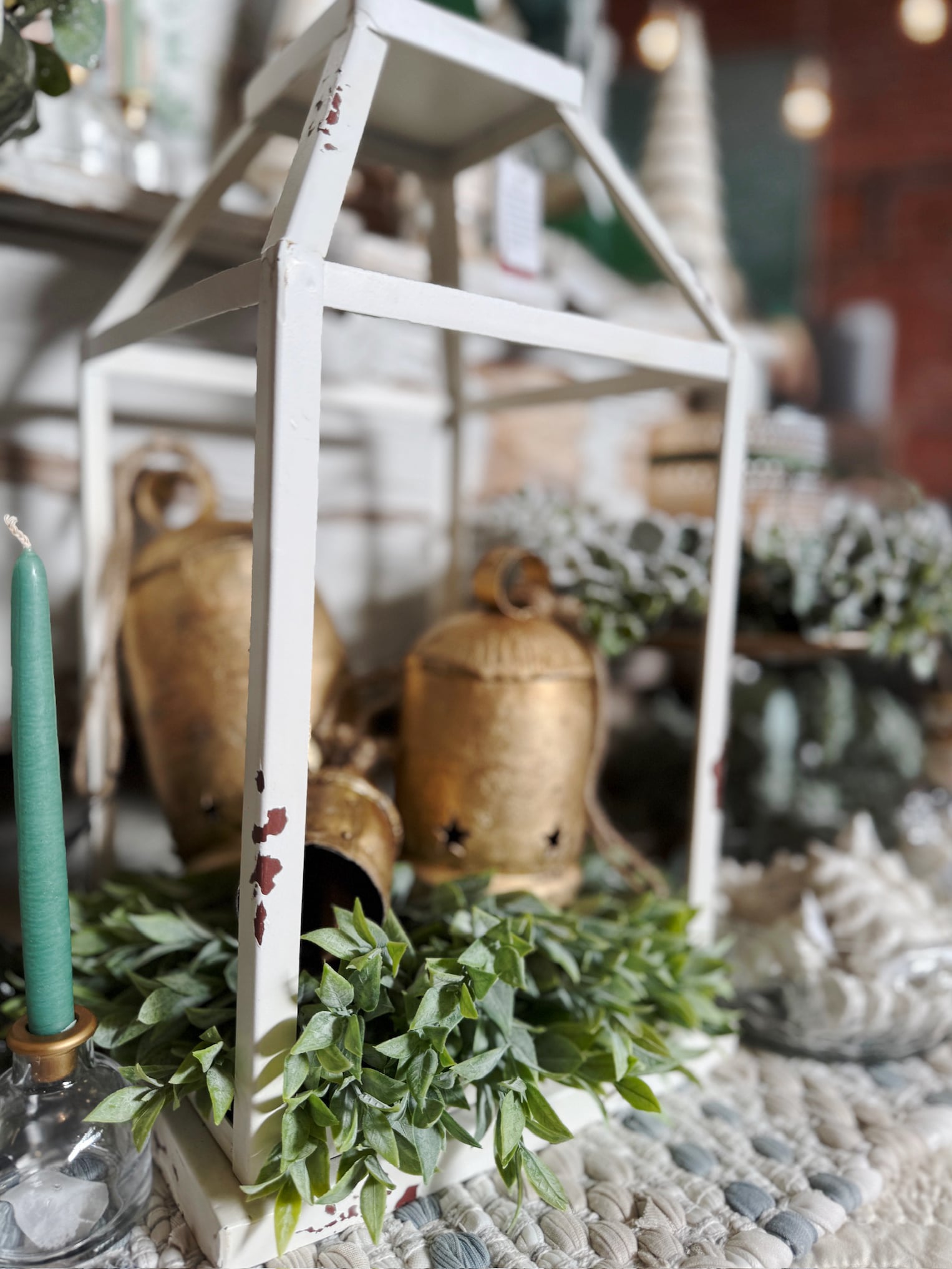 Antique brass star cut-out bells resting inside a distressed white lantern with powdered green stems.