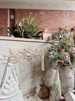 Embossed metal Christmas stockings wall sign styled with holiday greenery, a gold taper holder, and festive décor.