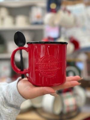 Close-up of a red Santa Certified mug with an embossed design and spoon tucked neatly into the handle slots.