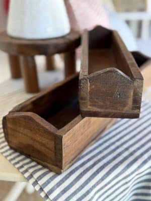 Two narrow, rustic wooden trays stacked on a blue striped table runner, showcasing their handcrafted texture and simple box-style shape.