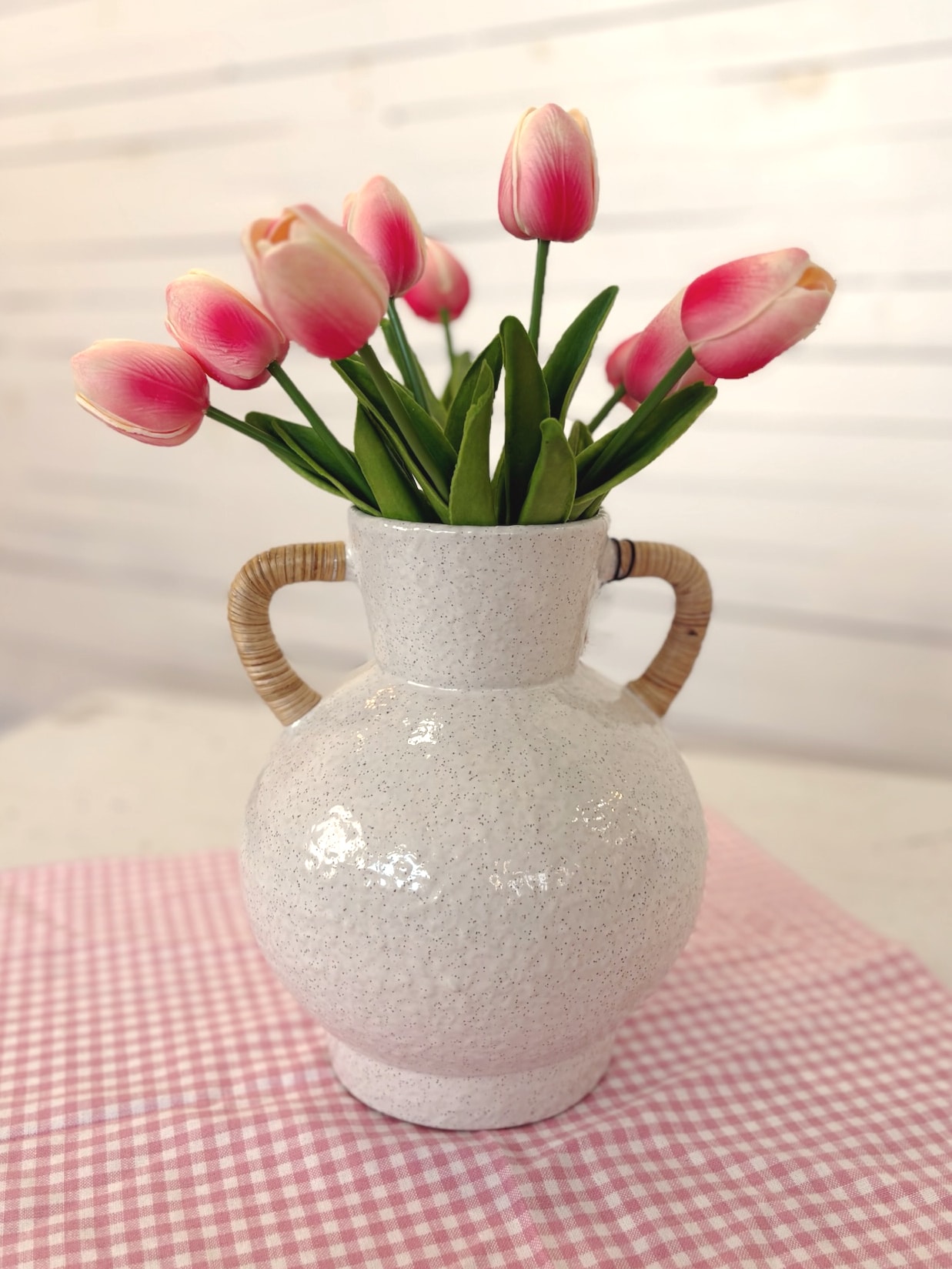 Bright Pink Tulip Bundle arranged in the Rattan Wrapped Handle Vase Medium on a pink gingham table runner.