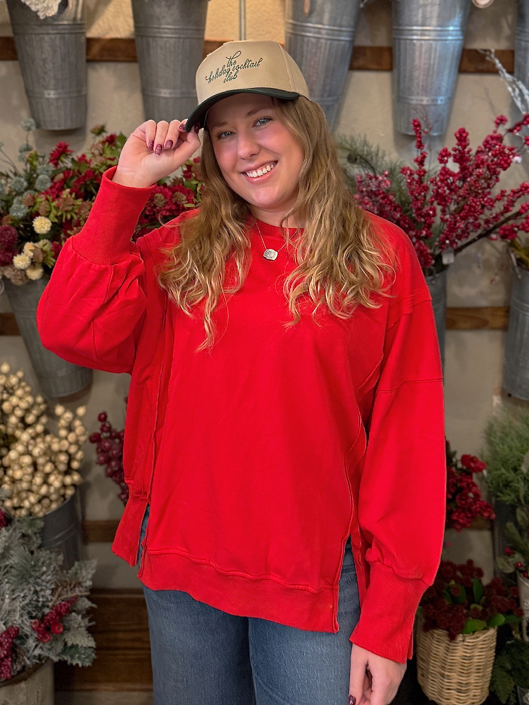 Smiling woman in a red oversized crewneck with ribbed cuffs and hem, posing among festive floral displays.