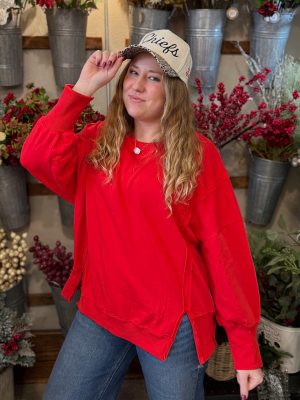 Woman wearing an oversized red crewneck with side slits and a natural-colored Chiefs trucker hat with a leopard-print bill.