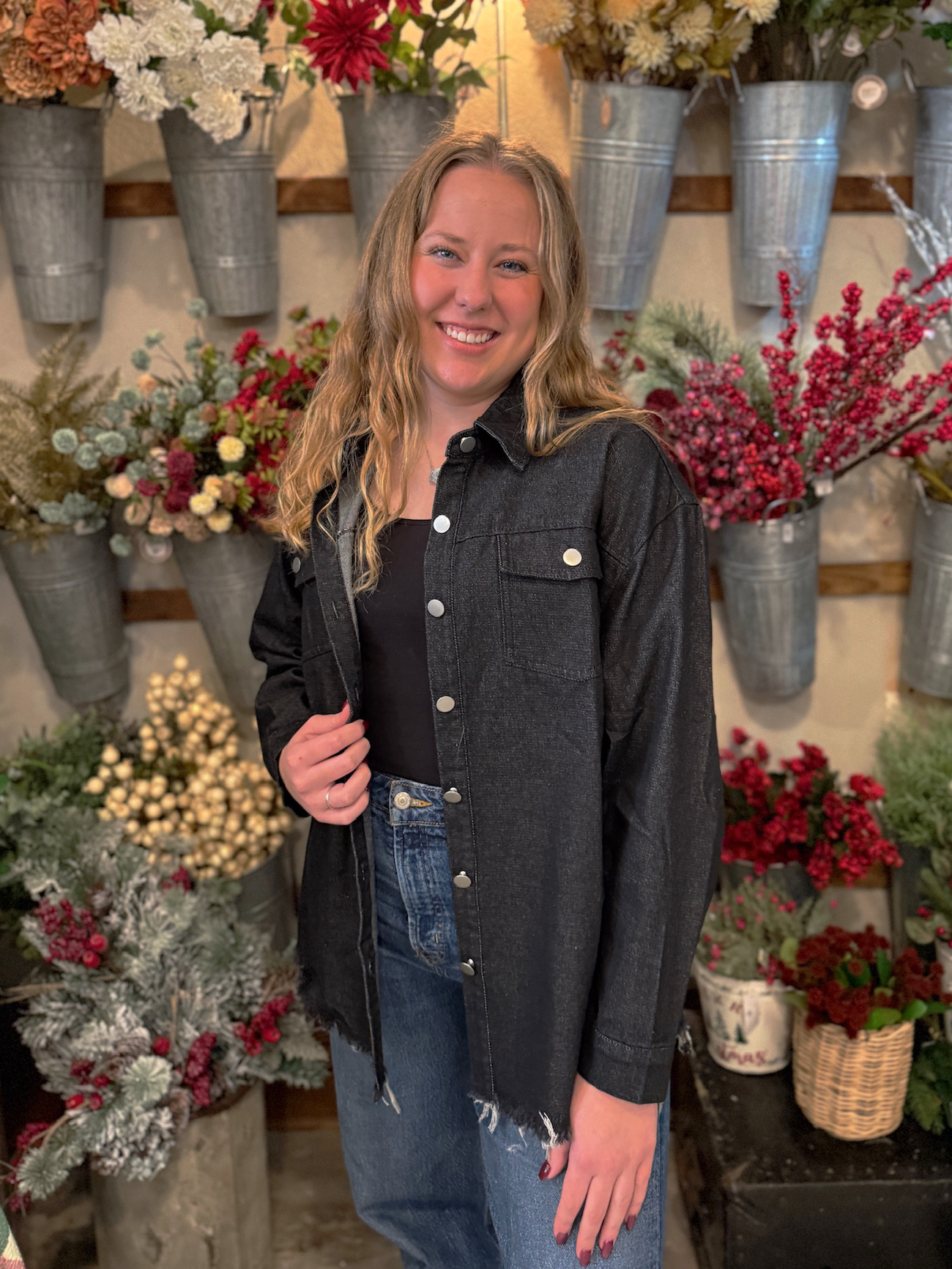 Model adjusting the collar of a black denim jacket featuring a relaxed fit and raw hem detail.