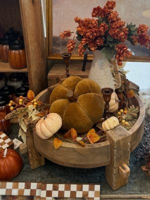 Rustic chakki pedestal with velvet pumpkin, foliage garland, and rattan vase filled with orange hops.