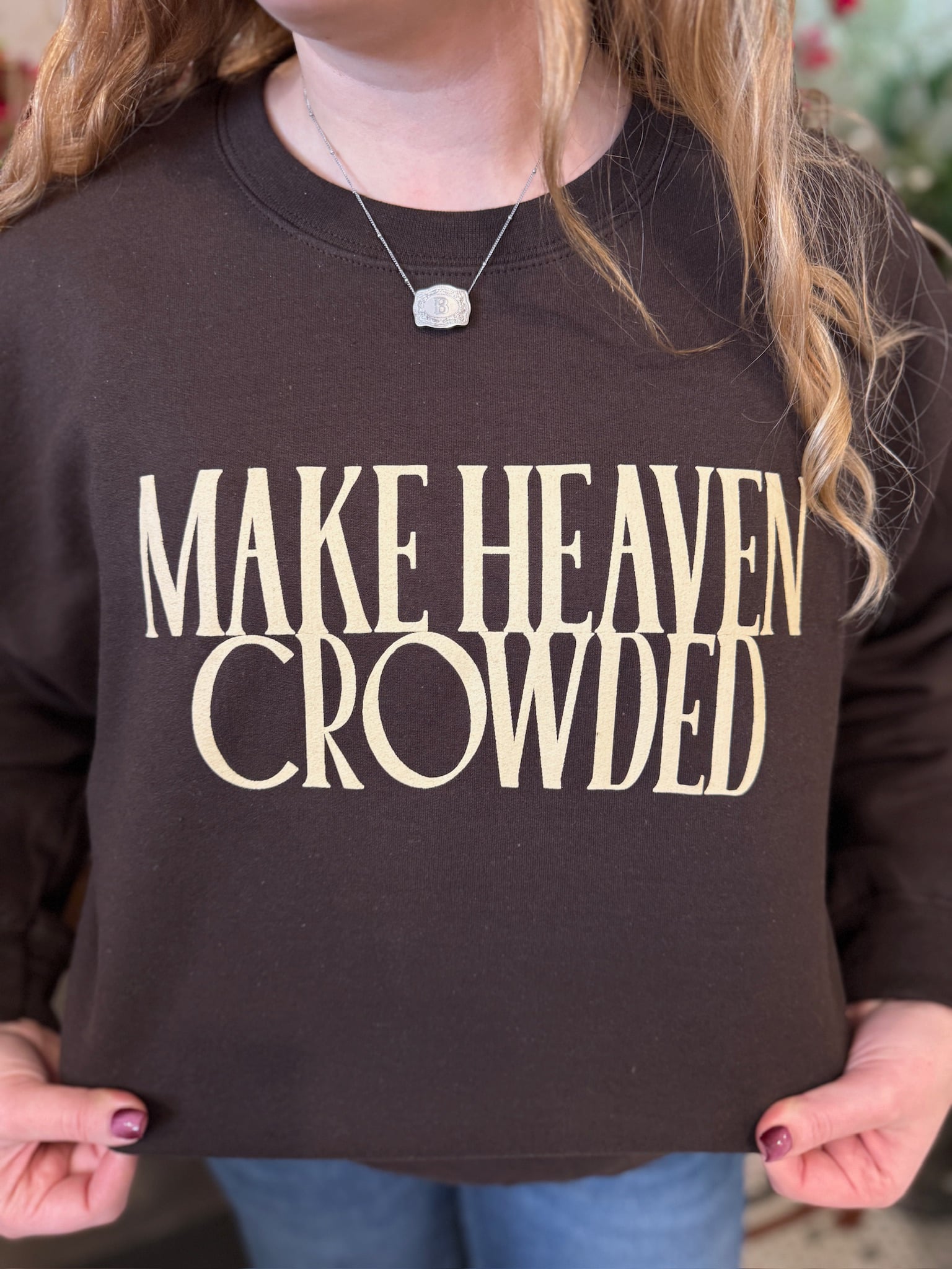Close-up view of the Make Heaven Crowded Crewneck showing the bold cream block lettering on the chocolate brown fleece sweatshirt.