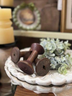 Aged wooden spools with distressed finish styled with greenery for farmhouse decor.