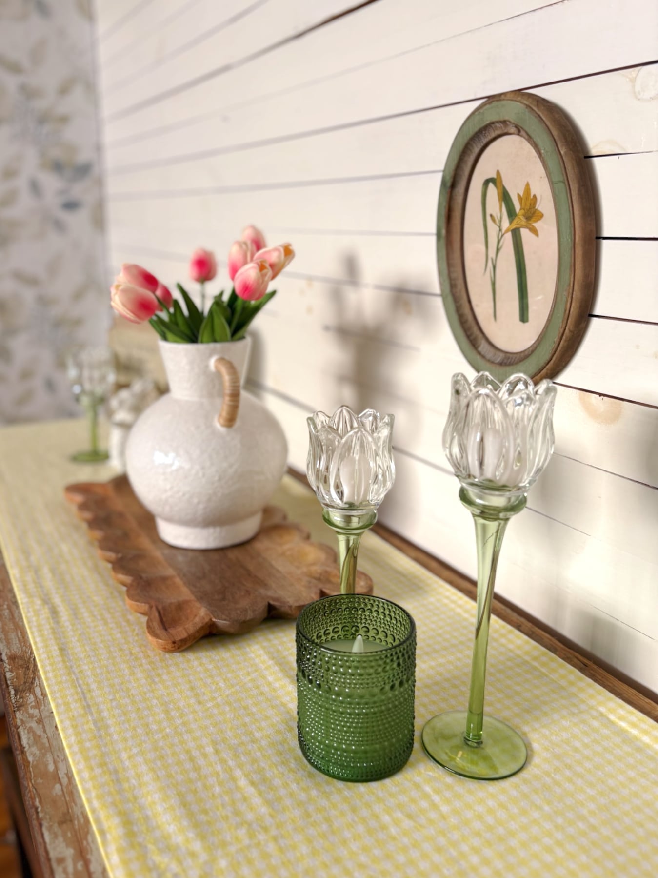 Small green dotted glass flameless candle styled with green tulip candle holders on a yellow gingham table runner.