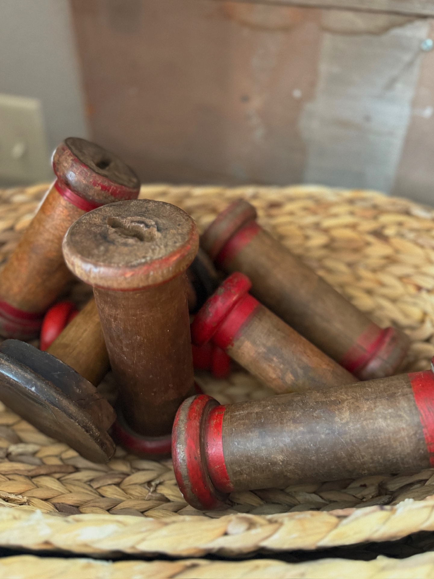 Vintage wooden spools with red accents styled on a woven tray for rustic home decor.