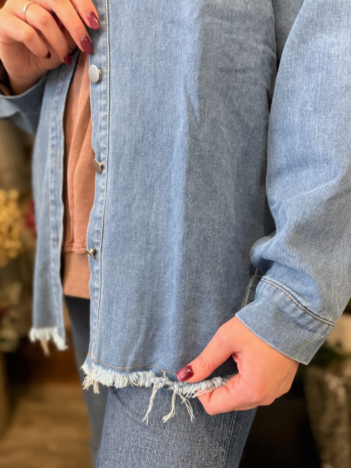 Woman wearing a washed blue denim jacket with a frayed hem, shown up close highlighting the raw edge detail and relaxed fit.