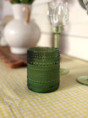 Small green dotted glass flameless candle styled on a yellow gingham table runner with soft cottage-style decor.